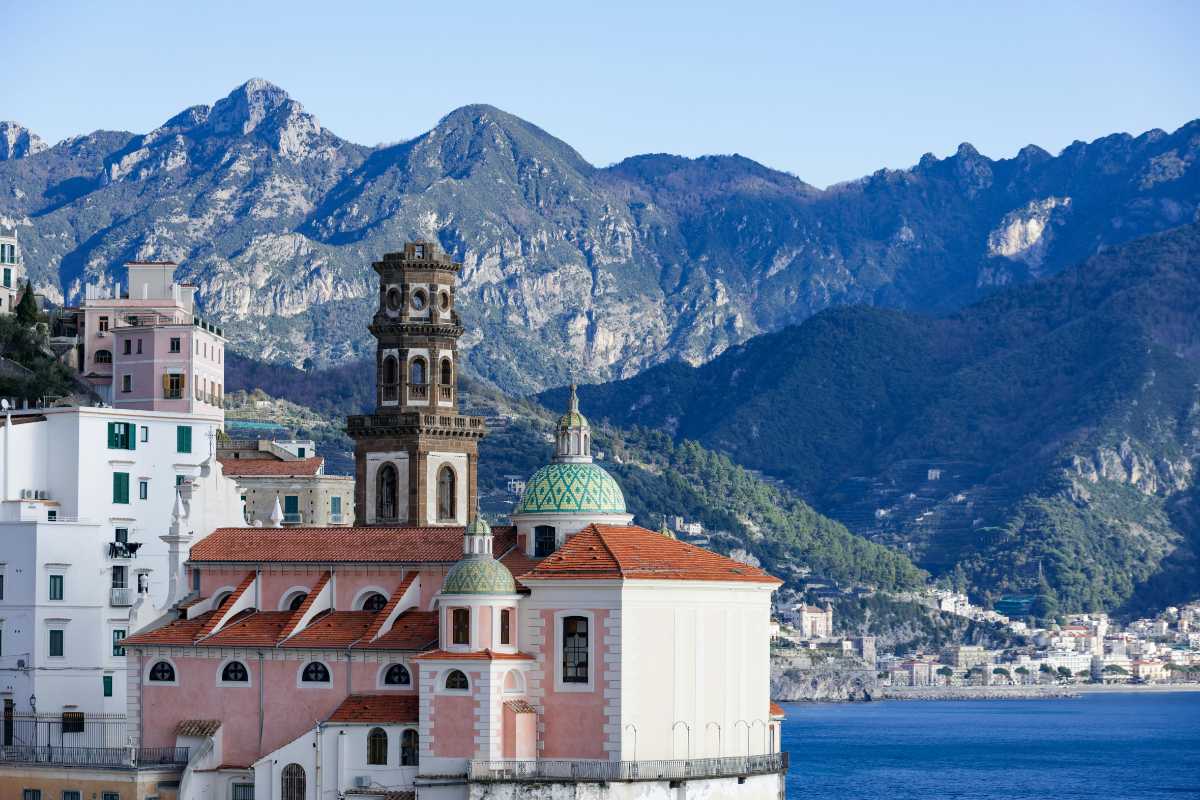 Vista panoramica di Amalfi con arrivo di viaggiatori, valigie, autobus e traghetti, atmosfera solare e accogliente