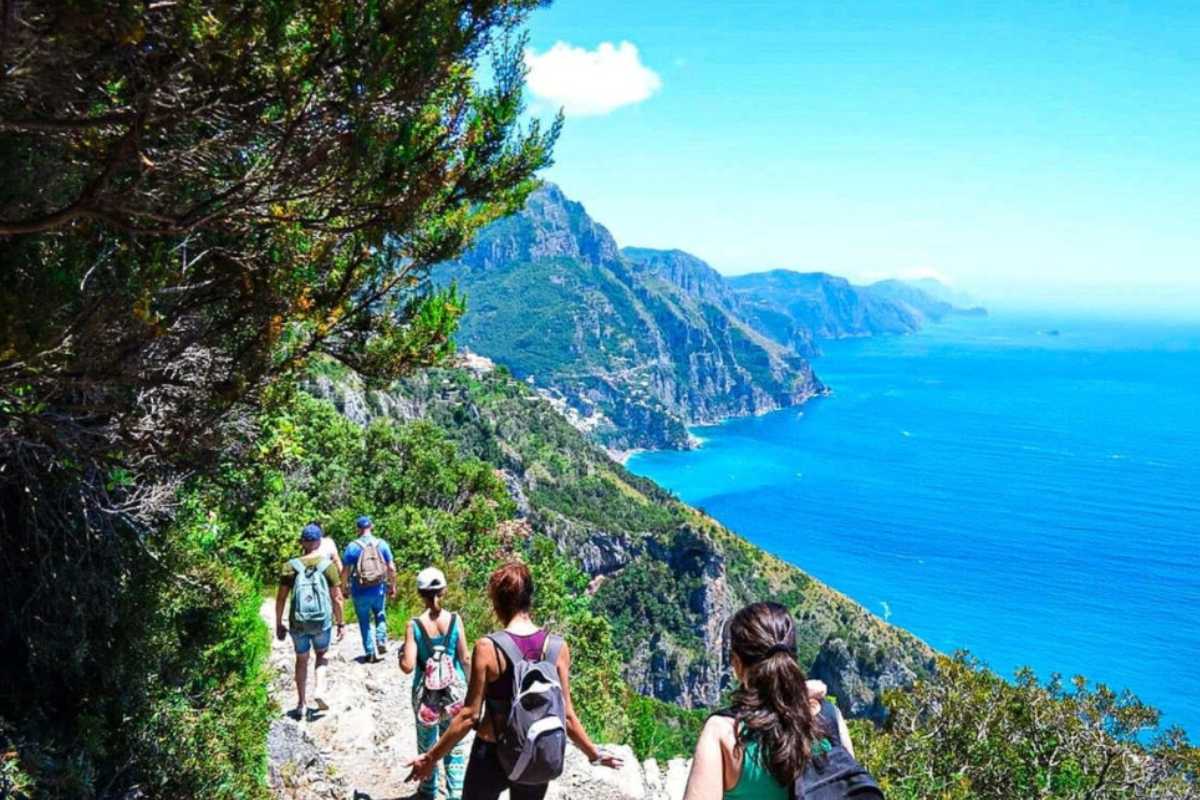 Famiglia con bambini che cammina lungo il Sentiero dei Limoni, terrazzamenti di limoni sullo sfondo, vista sul mare e sul borgo di Amalfi, atmosfera primaverile
