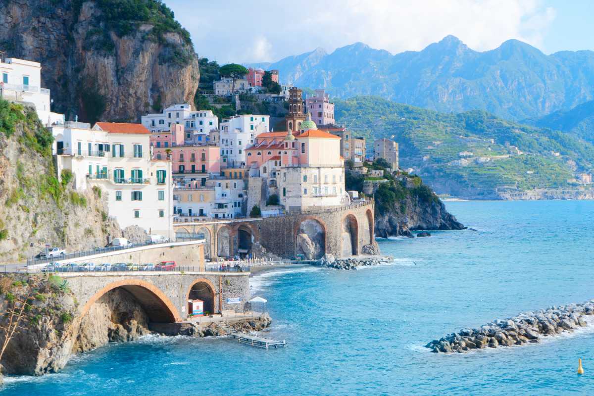 Scorcio panoramico di una spiaggia di Amalfi, vista dall’alto con mare turchese, ombrelloni colorati e le tipiche case bianche del centro storico sullo sfondo
